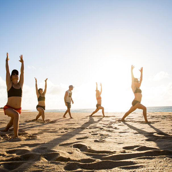 A group of friends enjoying some evening beach yoga while vacationing in Hawaii.